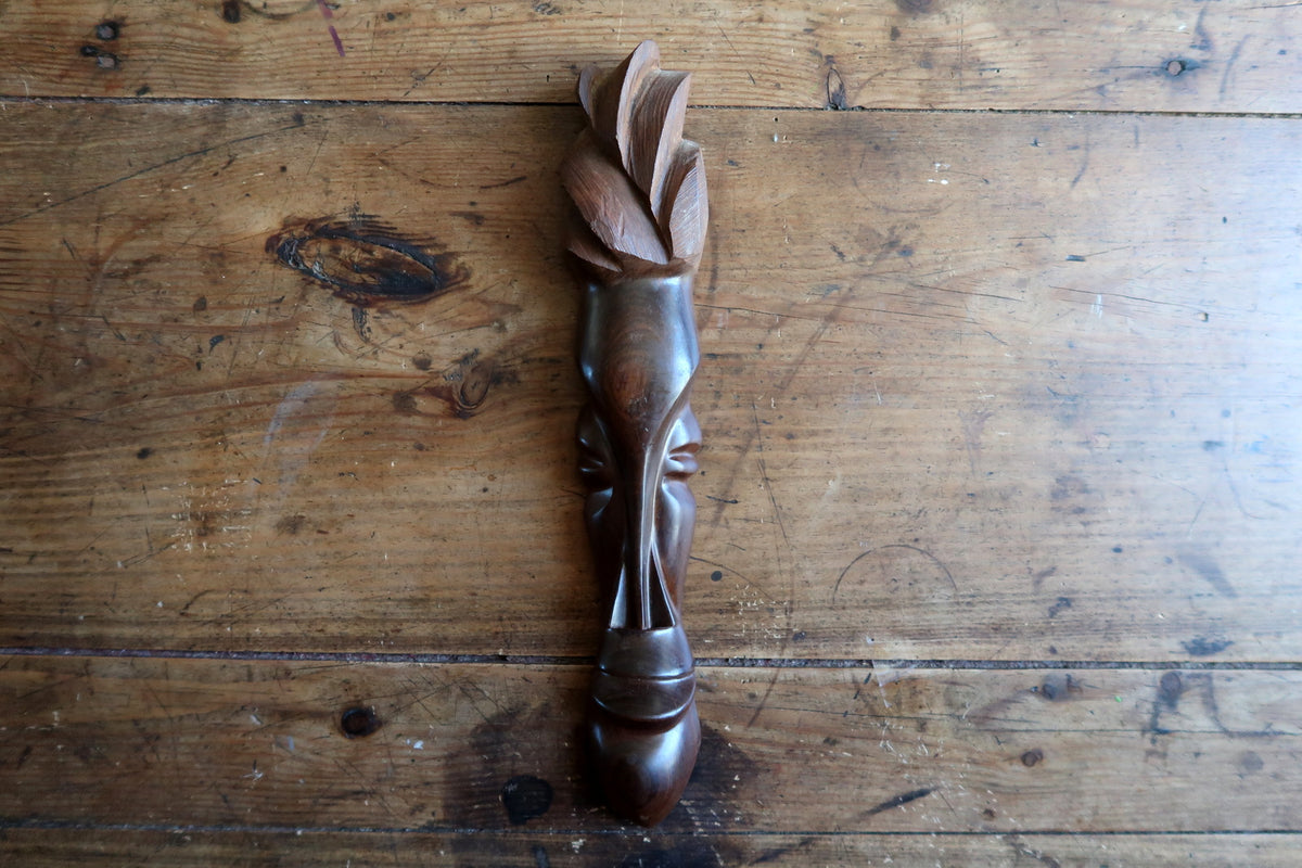 Three-quarter view highlighting the fluid polish, slender profile, and radiating leaf-petal crown of a hand-carved African hardwood wall sculpture.