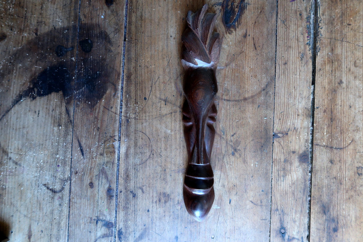 Detail close-up of the minimalist facial carving showing the smooth polished brown tropical hardwood, subtle nose ridge, and implied eye planes.