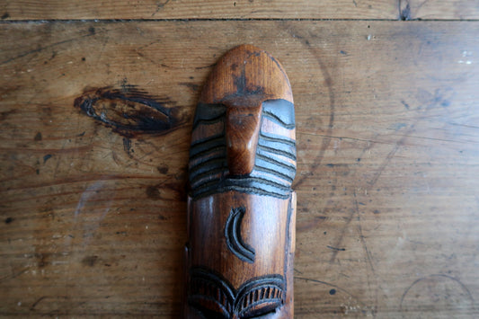 Three-quarter view highlighting the three-dimensional depth, smooth polish, and warm brown tones of a hand-carved African wooden mask sculpture.
