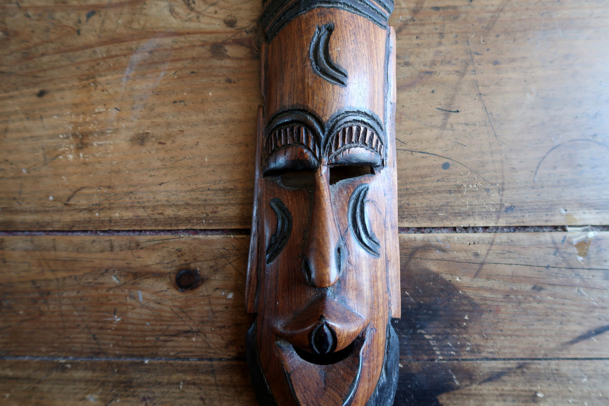 Close-up of the facial carving showing slit eyes, smooth brow planes, and a long slender nose carved from solid tropical hardwood.