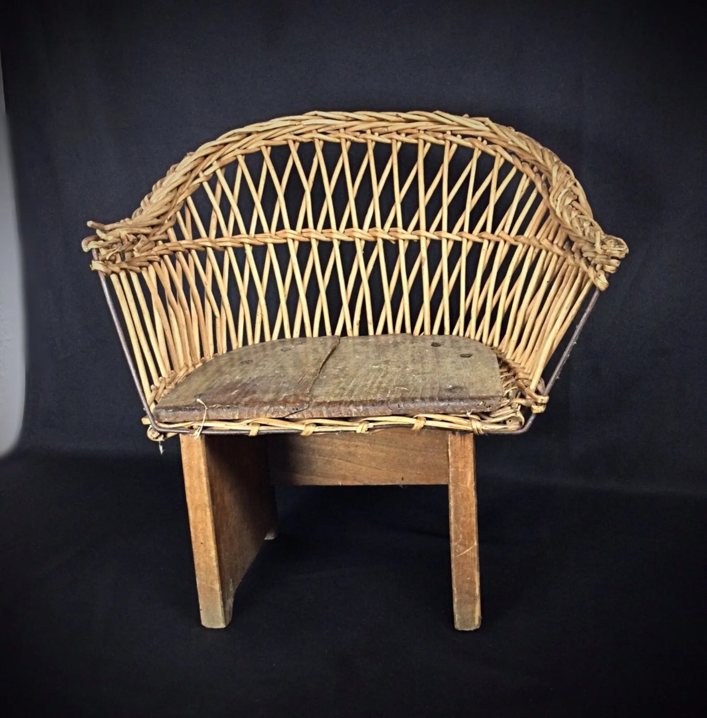 Early 1900s child-sized chair with rustic wood frame and woven wicker seat on display

