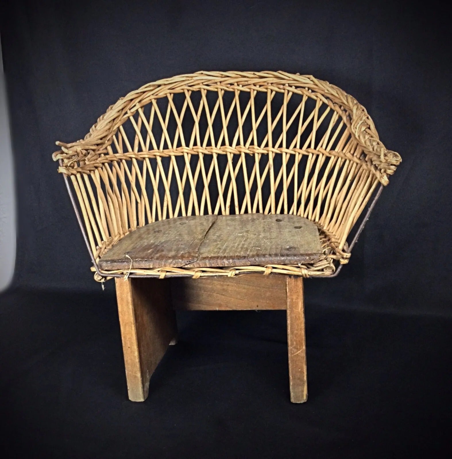 Early 1900s child-sized chair with rustic wood frame and woven wicker seat on display

