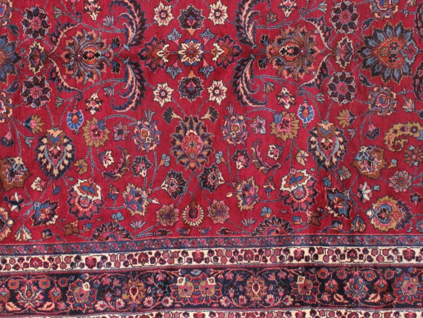 Antique Persian Mashad rug in original good condition. The field of the rug is in red shade with floral design and navy blue border. 