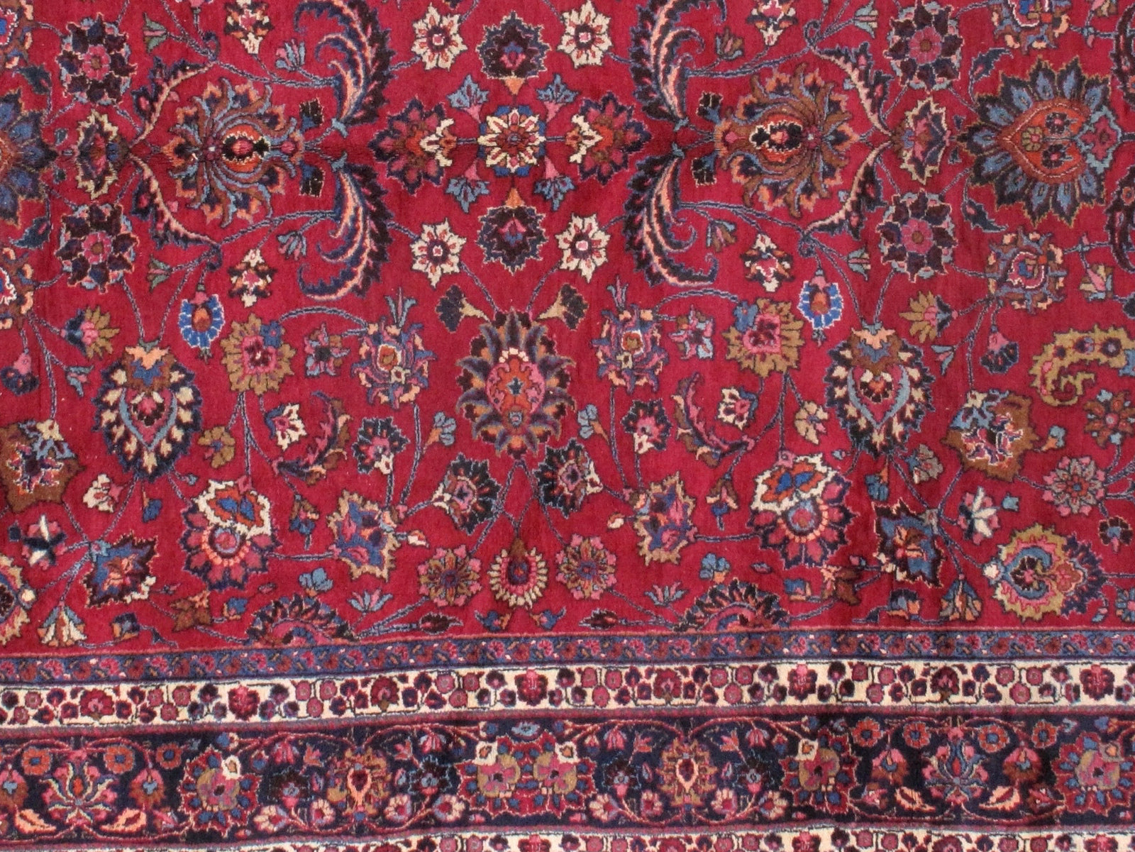 Antique Persian Mashad rug in original good condition. The field of the rug is in red shade with floral design and navy blue border. 