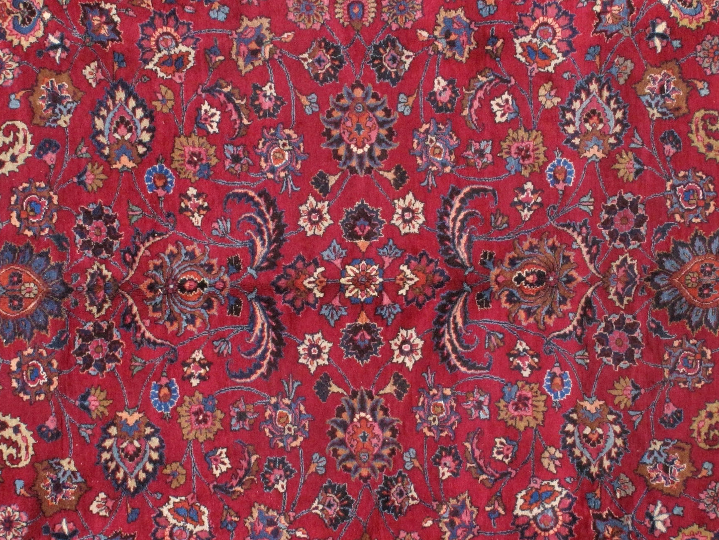 Antique Persian Mashad rug in original good condition. The field of the rug is in red shade with floral design and navy blue border. 