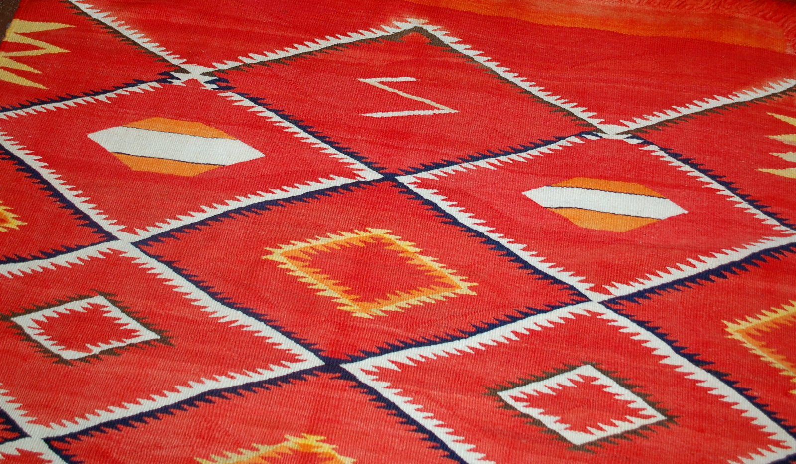 Antique hand-woven American-Indian Navajo blanket in original good condition. The blanket has been made in the end of 19th century in bright red shade. Repeating diamonds are in white and indigo shades. Smaller inner diamonds are in yellow and orange.