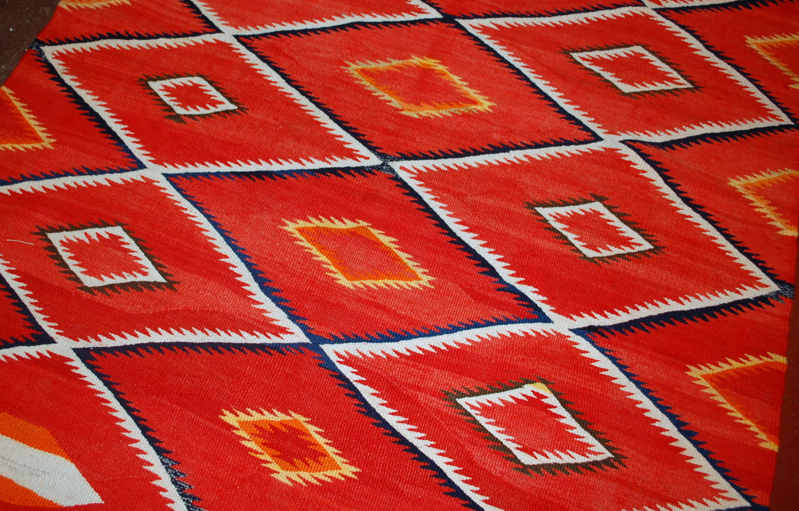 Antique hand-woven American-Indian Navajo blanket in original good condition. The blanket has been made in the end of 19th century in bright red shade. Repeating diamonds are in white and indigo shades. Smaller inner diamonds are in yellow and orange.