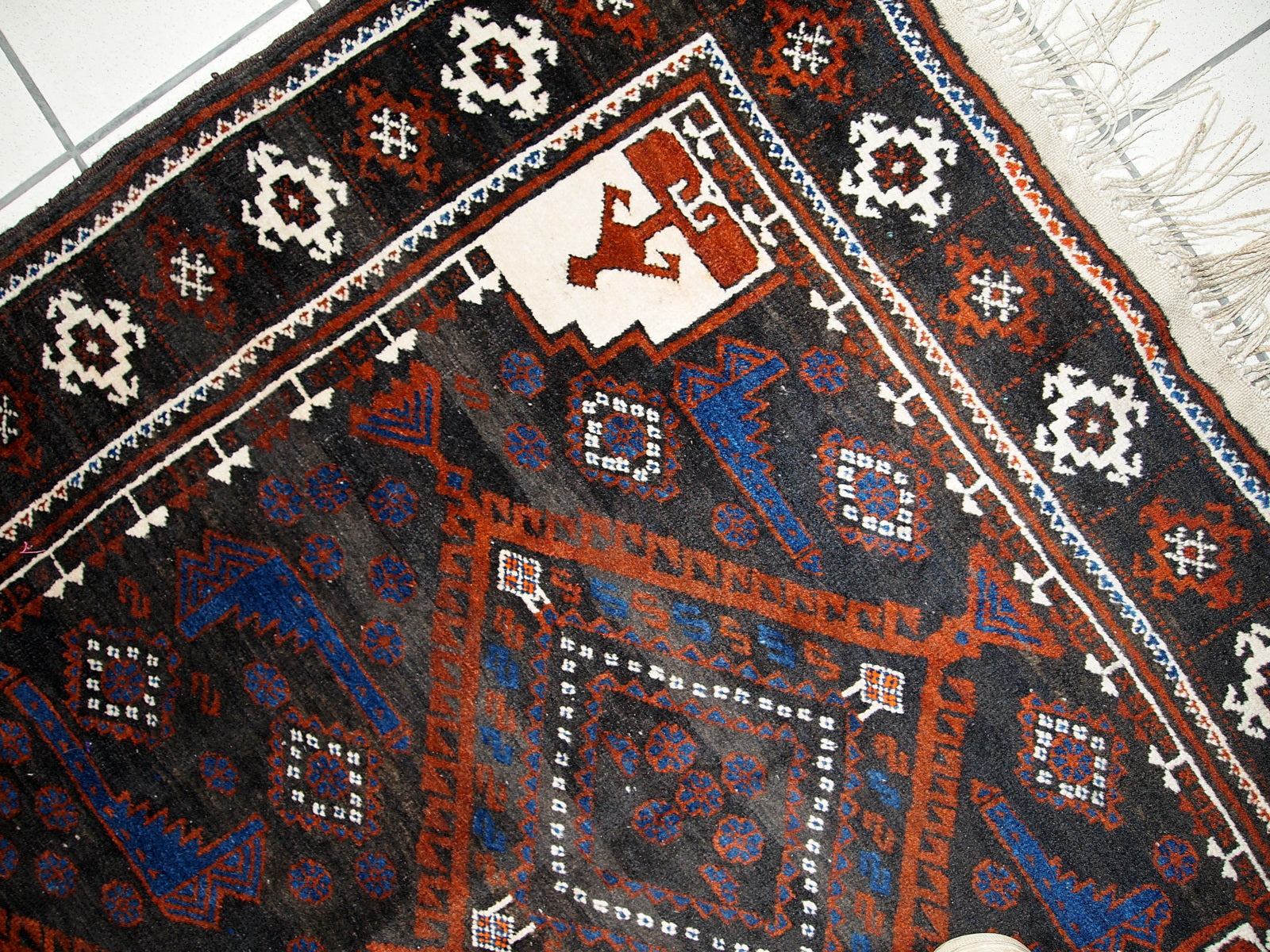 Close-up of intricate tribal figures in rusty red on the Afghan rug.