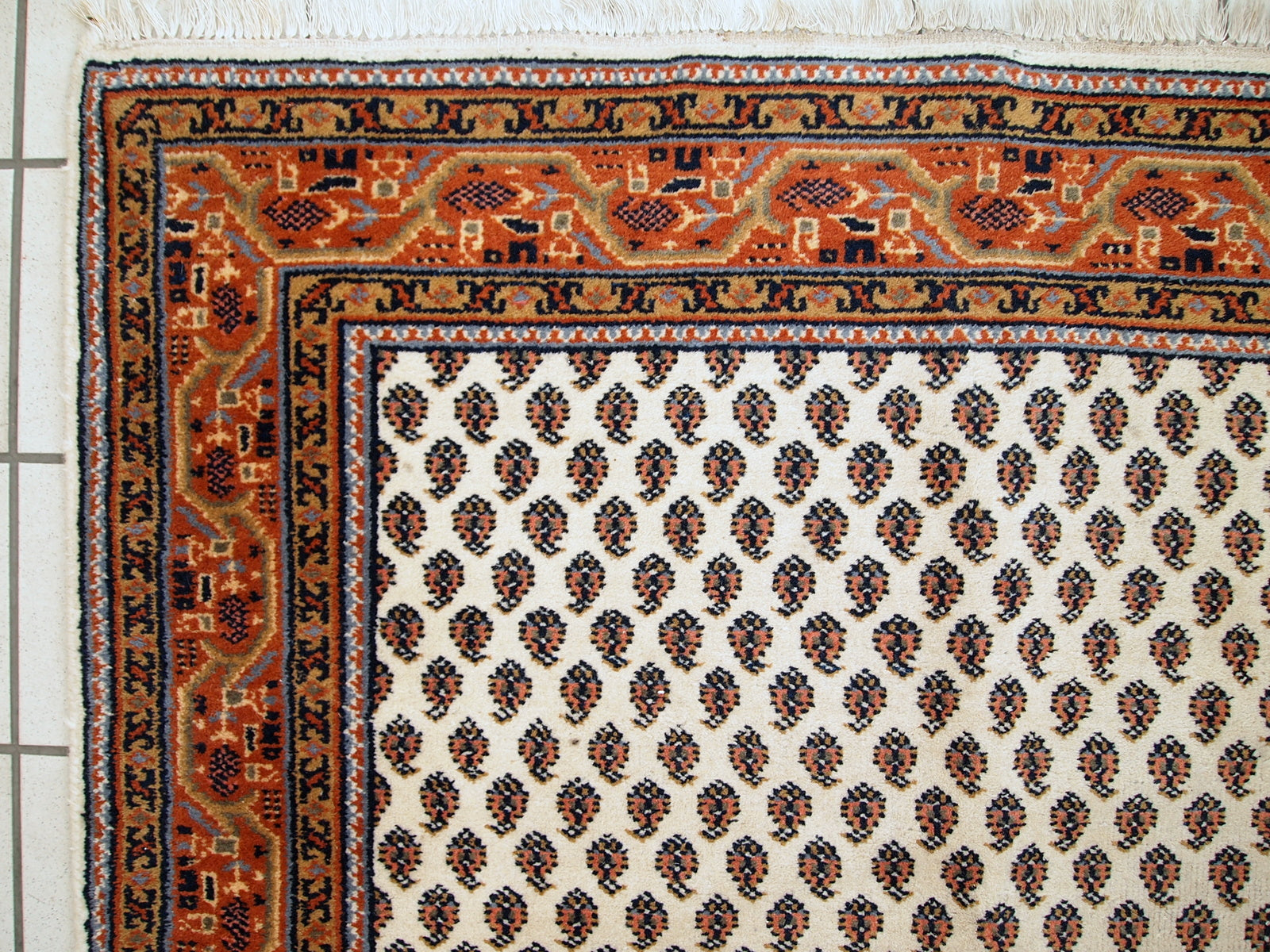 Vintage handmade Indian rug with Seraband design in white shade with rusty border. All-over design with paisley pattern. The rug is from the end of 20th century in original good condition.  