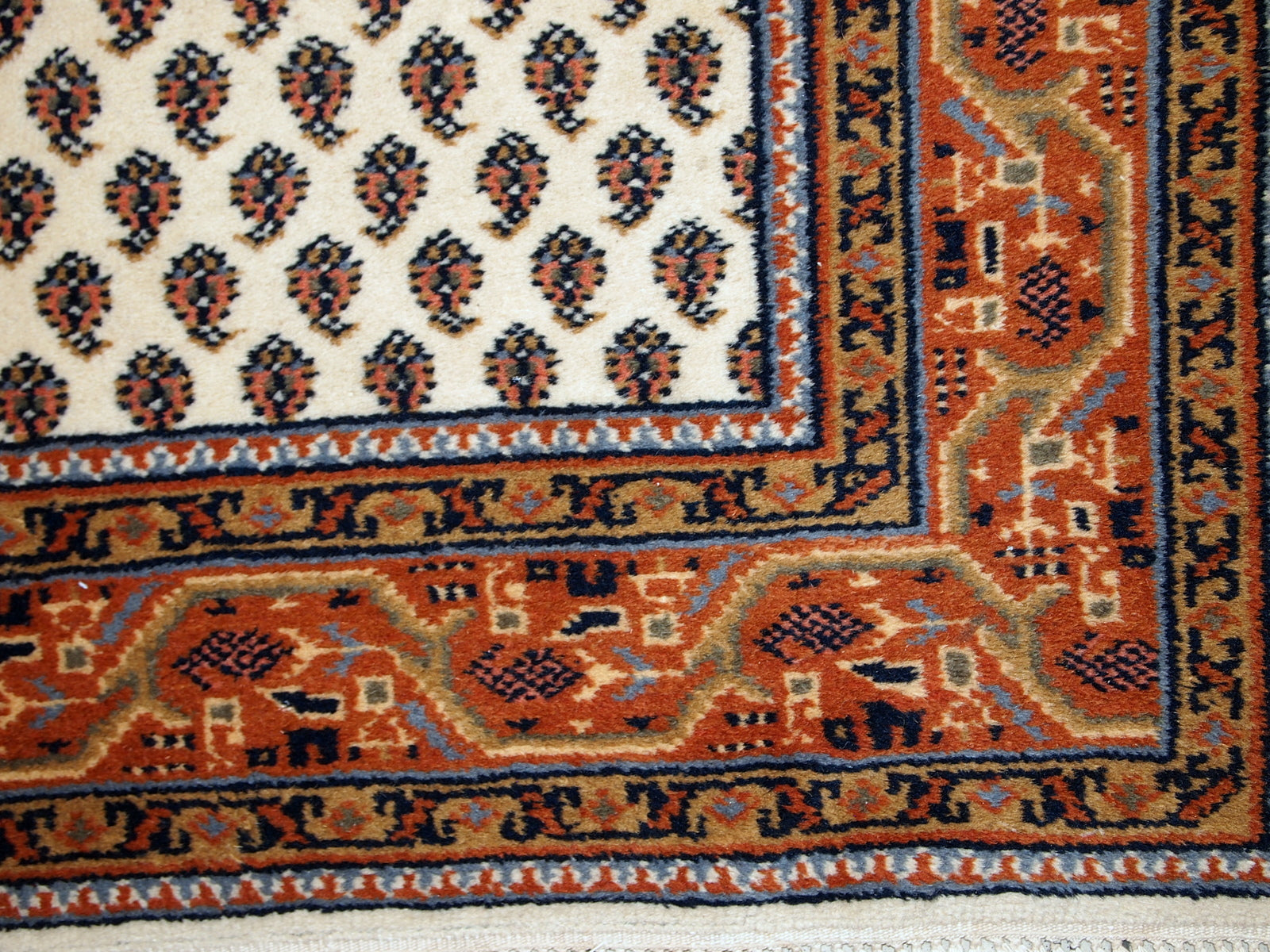 Vintage handmade Indian rug with Seraband design in white shade with rusty border. All-over design with paisley pattern. The rug is from the end of 20th century in original good condition.  