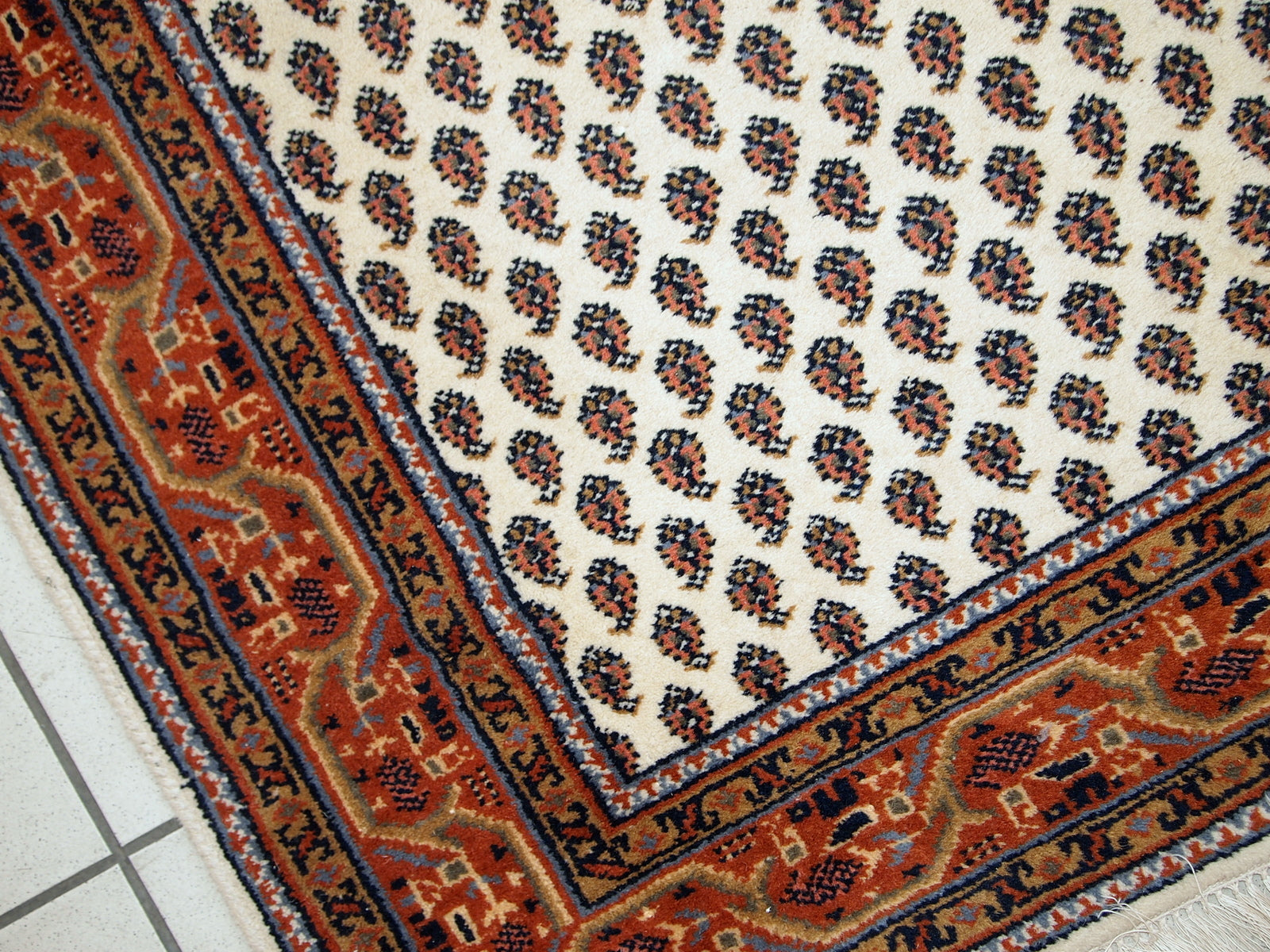 Vintage handmade Indian rug with Seraband design in white shade with rusty border. All-over design with paisley pattern. The rug is from the end of 20th century in original good condition.  
