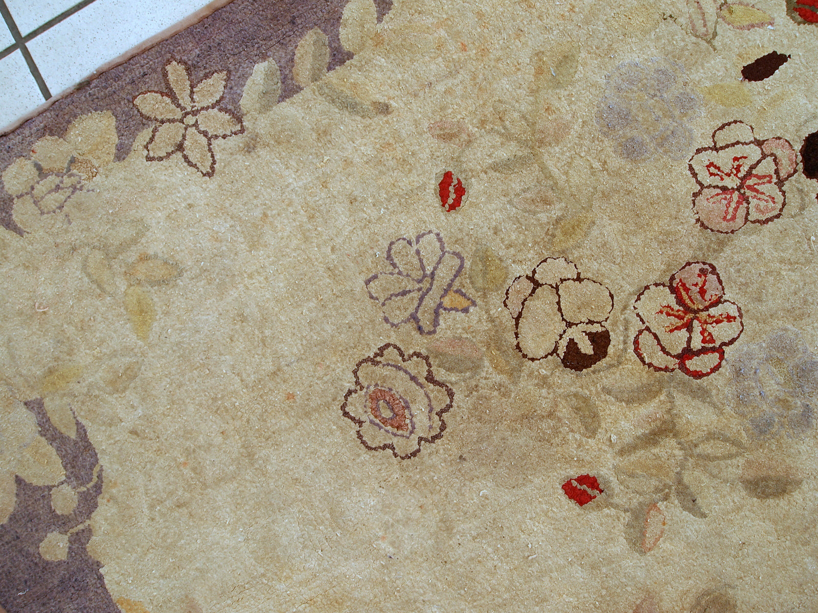 Handmade antique American Primitive Hooked rug in beige shade with abstract/floral design. The border is purple. It is in good condition.