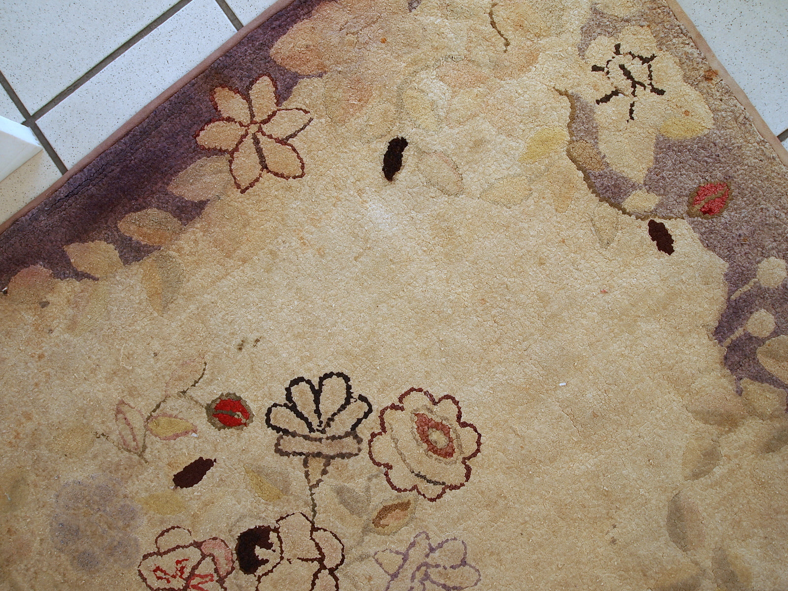 Handmade antique American Primitive Hooked rug in beige shade with abstract/floral design. The border is purple. It is in good condition.