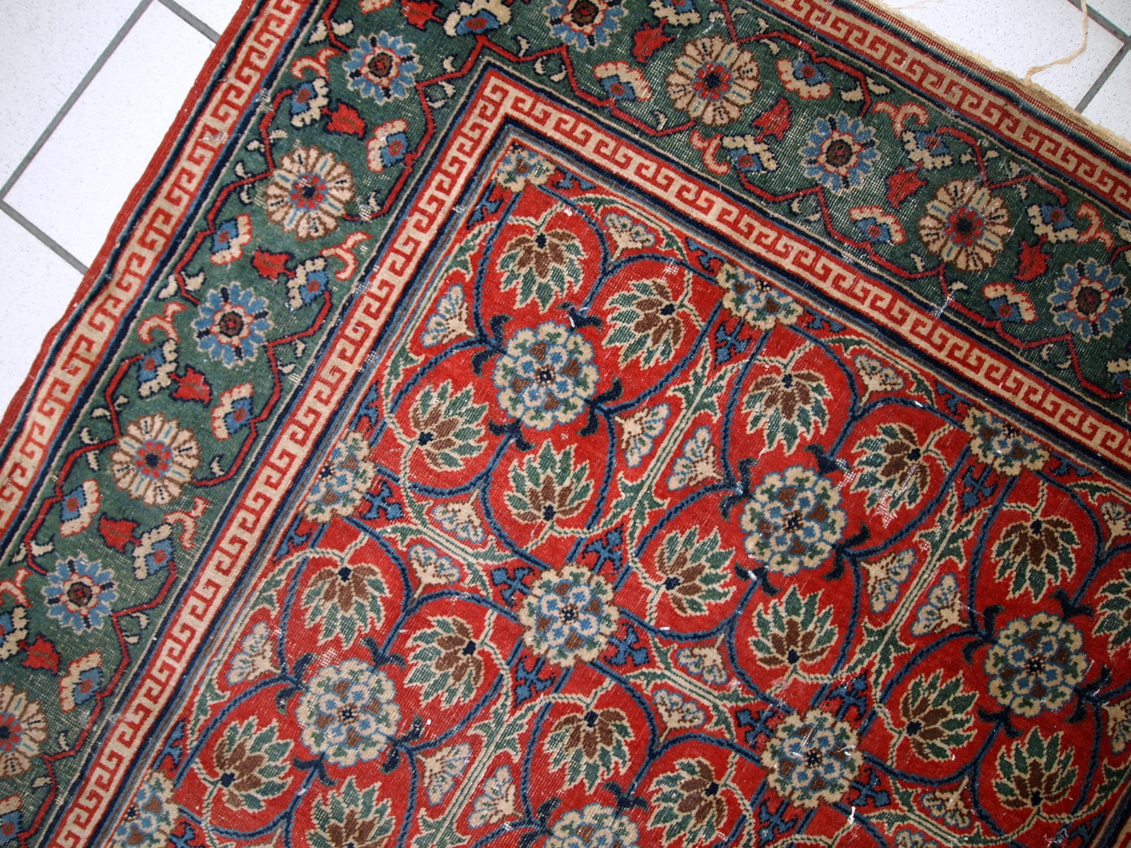 Handmade antique East Turkestan distressed rug with repeating pattern. It is in red and green shades, made in the beginning of 20th century.
