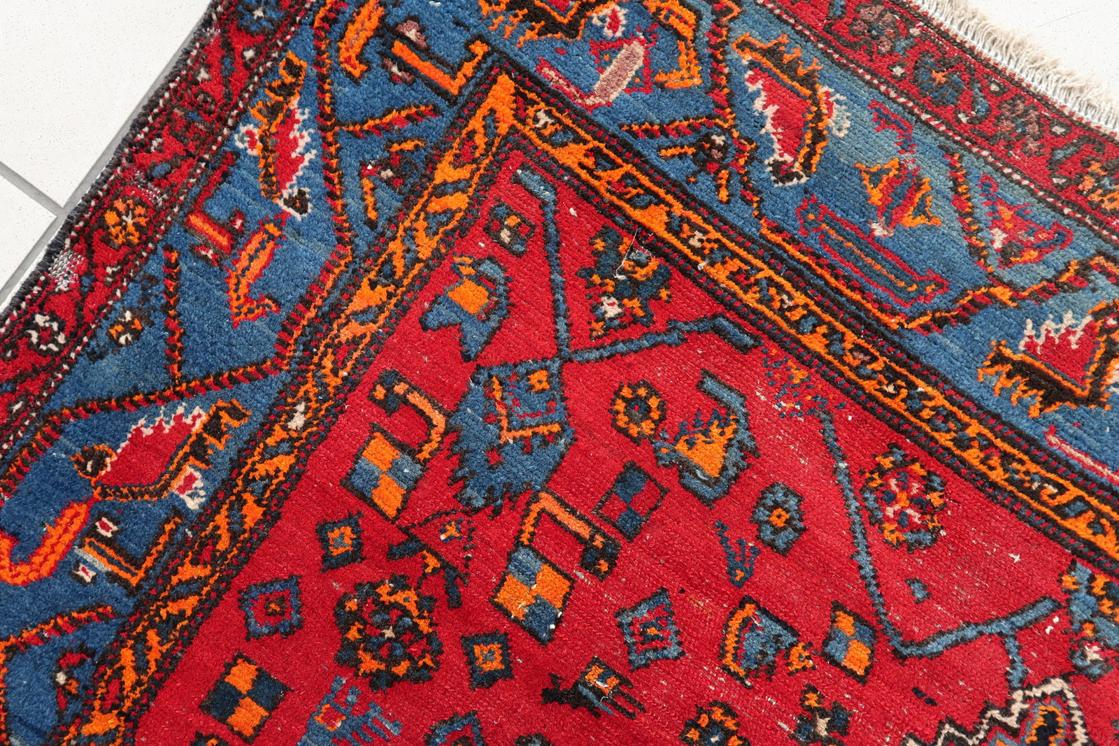 Handmade vintage Middle Eastern rug in red and blue shades. The rug has been made in wool in the middle of 20th century. It is in original condition, it has some low pile. The design on the rug is unusual, medallion is not even.